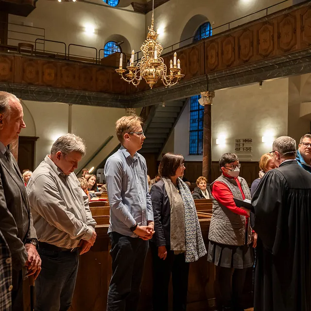 Eine Gruppe von Personen steht in einer Kirche und lauscht einer Ansprache.