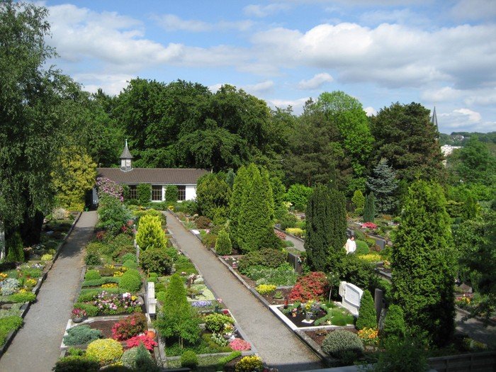 Ein Friedhof mit vielen Gräbern und Bäumen, im Hintergrund ein weißes Gebäude.