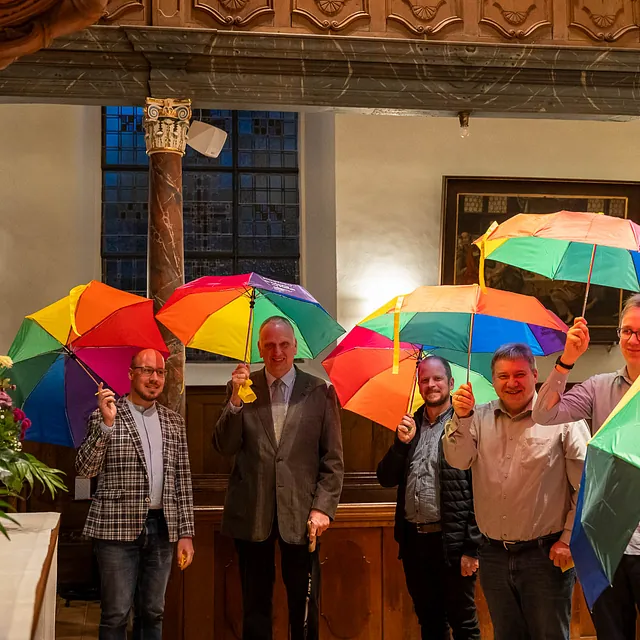 Gruppe von Personen posiert in einer Kirche mit bunten Regenschirmen.