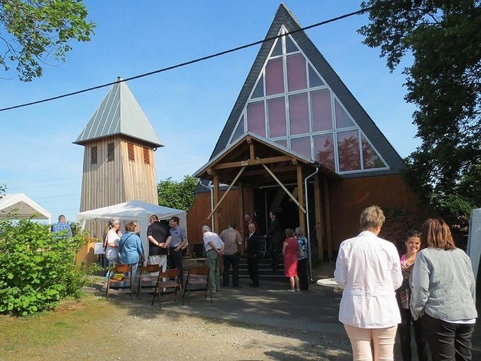 Moderne Kirche mit Glasgiebel, Holzturm, Menschen und Zelten.