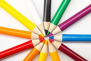Farbige Buntstifte im Kreis angeordnet, ein blauer Stift ragt heraus.