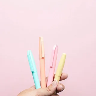 Nahaufnahme von drei pastellfarbenen Stiften auf rosa Hintergrund.
