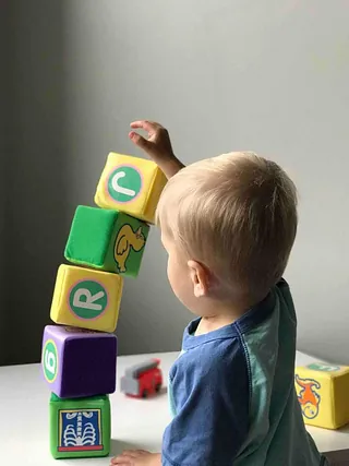Kleinkind mit blonden Haaren spielt mit bunten Buchstabenwürfeln.