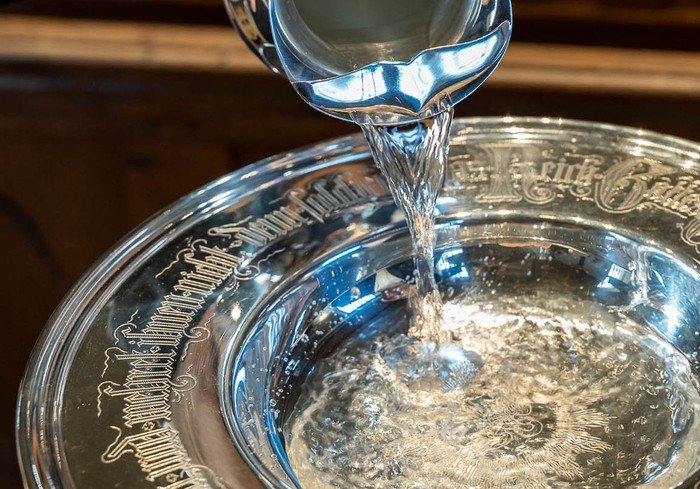 Wasser wird in ein silbernes Taufbecken gegossen.