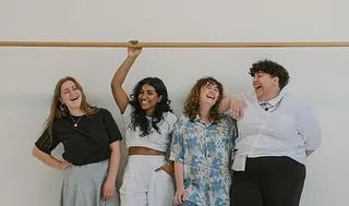 Eine Gruppe lachender junger Frauen lehnt an einer Holzstange.
