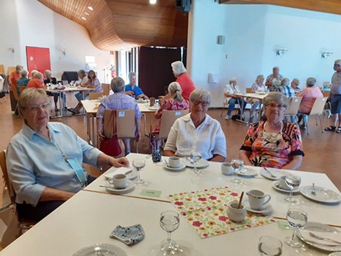 Ältere Personen mit Kaffee und Gebäck in hellem Raum.