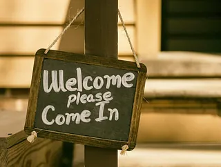 Schwarzes Schild mit Kreideaufschrift "Welcome Please Come In".