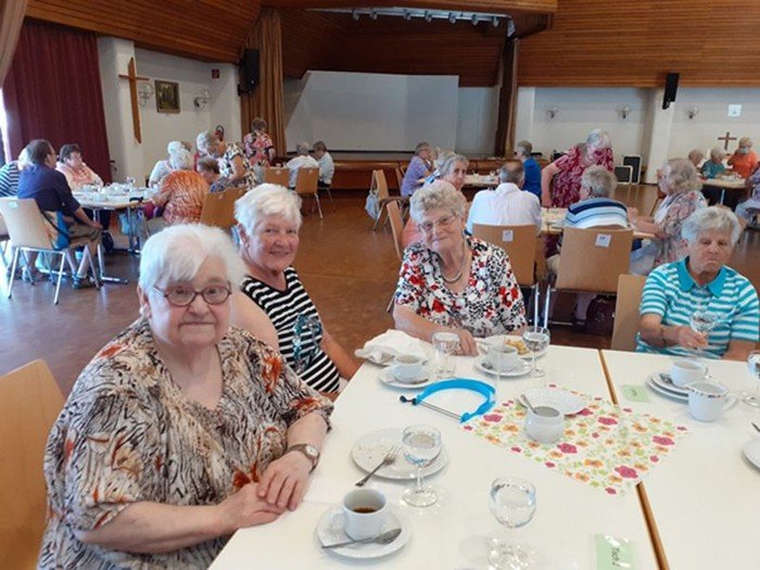 Ältere Damen an Tischen im Gemeinschaftsraum, teils lächelnd zur Kamera.