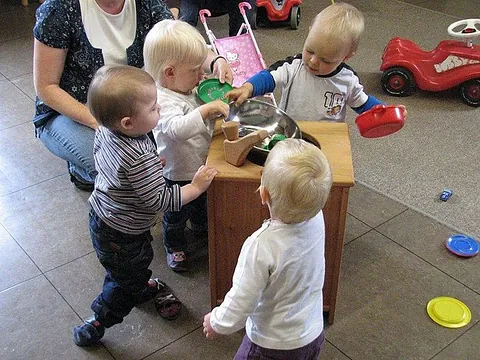 Kleinkinder spielen in einem Raum mit einer Betreuungsperson.