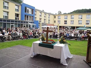 Open-Air-Gottesdienst vor Altenzentrum mit Kreuz und vielen Teilnehmenden.