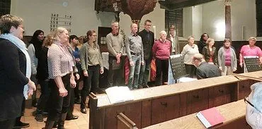 Eine Gruppe von Erwachsenen steht in einer Kirche und singt oder probt.