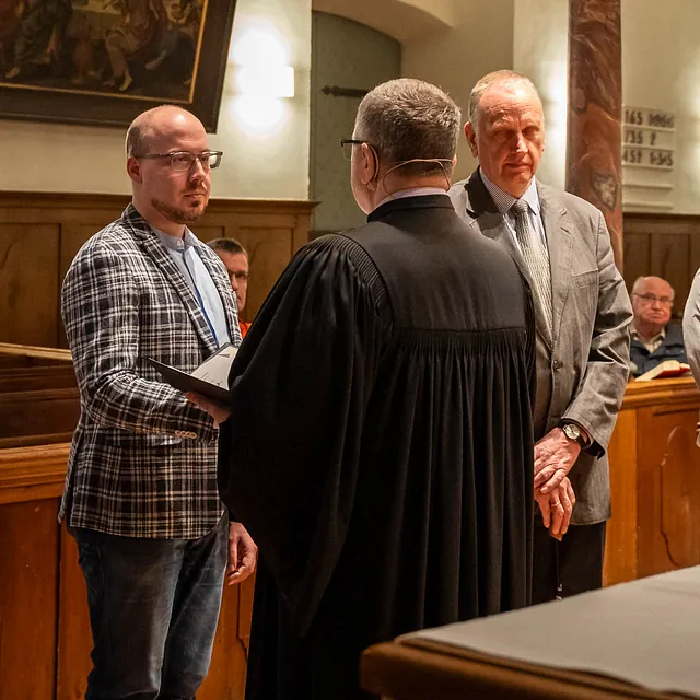 Männer in Anzügen und Talaren stehen in einer Kirche zusammen.