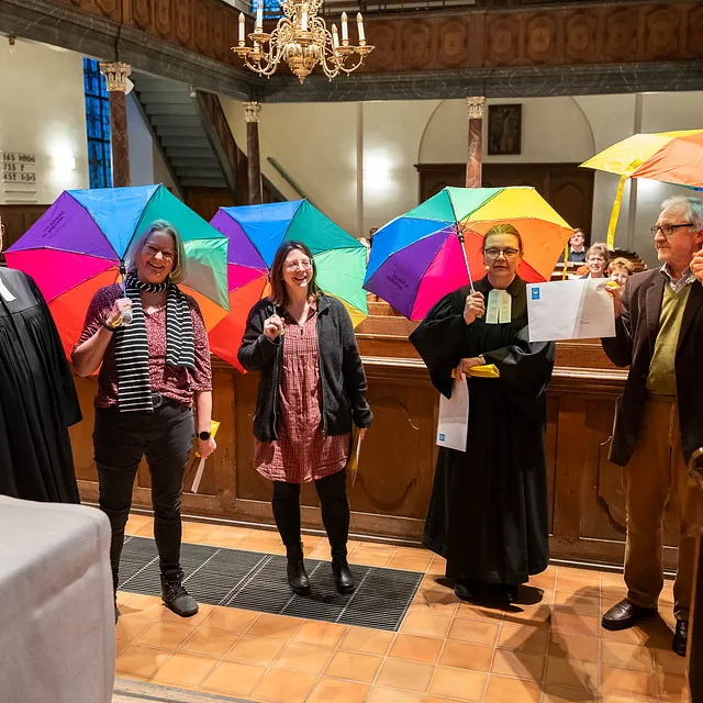 Gruppe von Personen mit bunten Regenschirmen in einer Kirche.