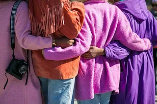 Umarmung zweier Personen mit lila Umhang und brauner Jacke.