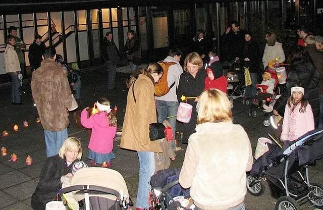 Menschenmenge mit Kindern und Lichtern im Freien bei Nacht.