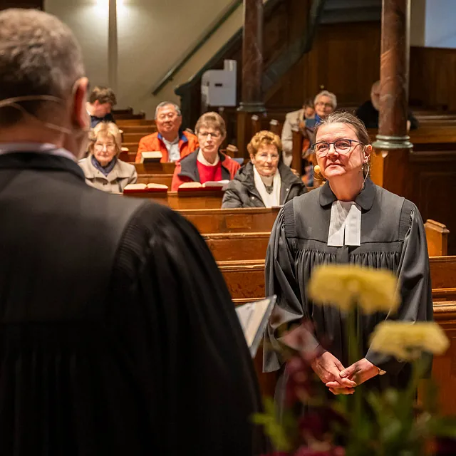 Eine Predigerin steht vor der Gemeinde in einer Kirche.